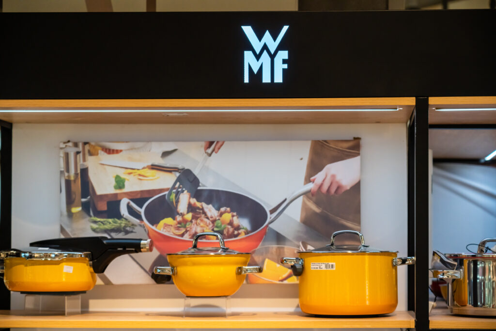 WMF Logo über einem Schaufenster in dem viele Töpfe in gelb und ein Wok in orange zu sehen sind